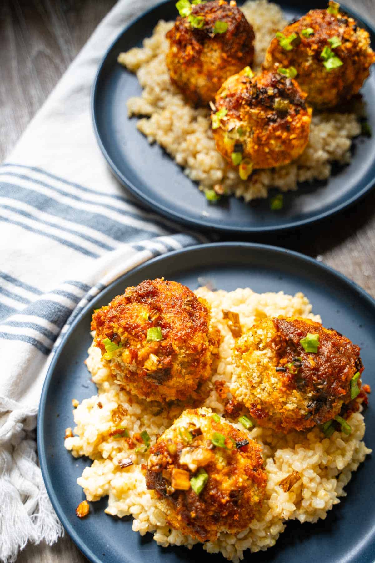 Asian eggplant meatballs with gochujang glaze on a bed of brown rice on blue plates.