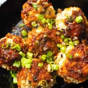 Asian eggplant meatballs with gochujang glaze in a black cast iron skillet garnished with raw and fried scallions.