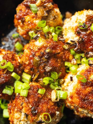 Asian eggplant meatballs with gochujang glaze in a black cast iron skillet garnished with raw and fried scallions.