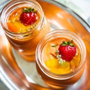 Easy Strawberry and Heirloom Gazpacho in individual sized mason jars on a silver plater held by a women in a flower dress.