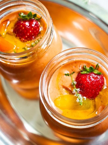 Easy Strawberry and Heirloom Gazpacho in individual sized mason jars on a silver plater held by a women in a flower dress.