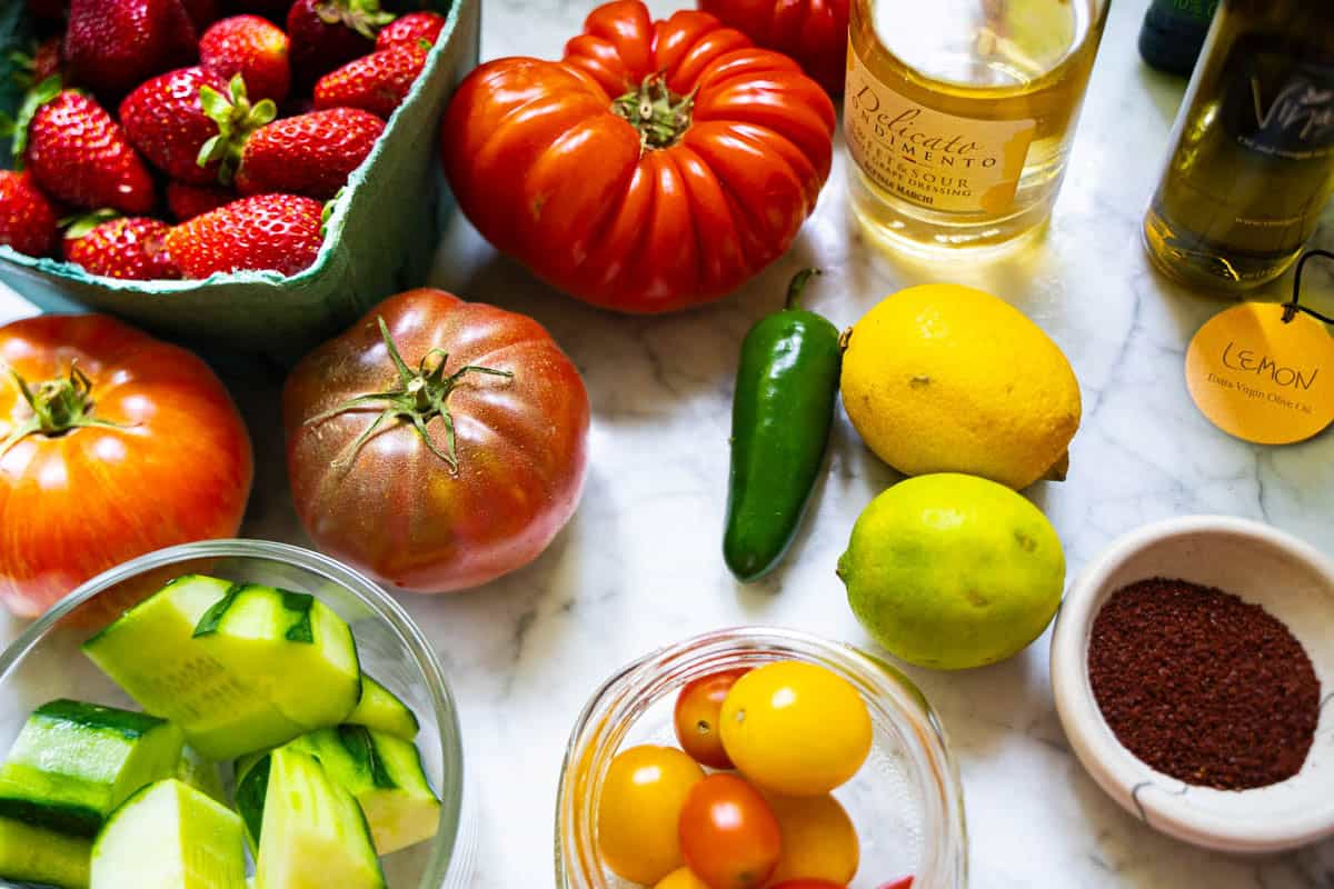 Easy Strawberry and Heirloom Tomato Gazpacho ingredients on a white marble counter.