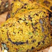 Gluten free zucchini bread sliced on a wooden cutting board next to a small vase of purple flowers.