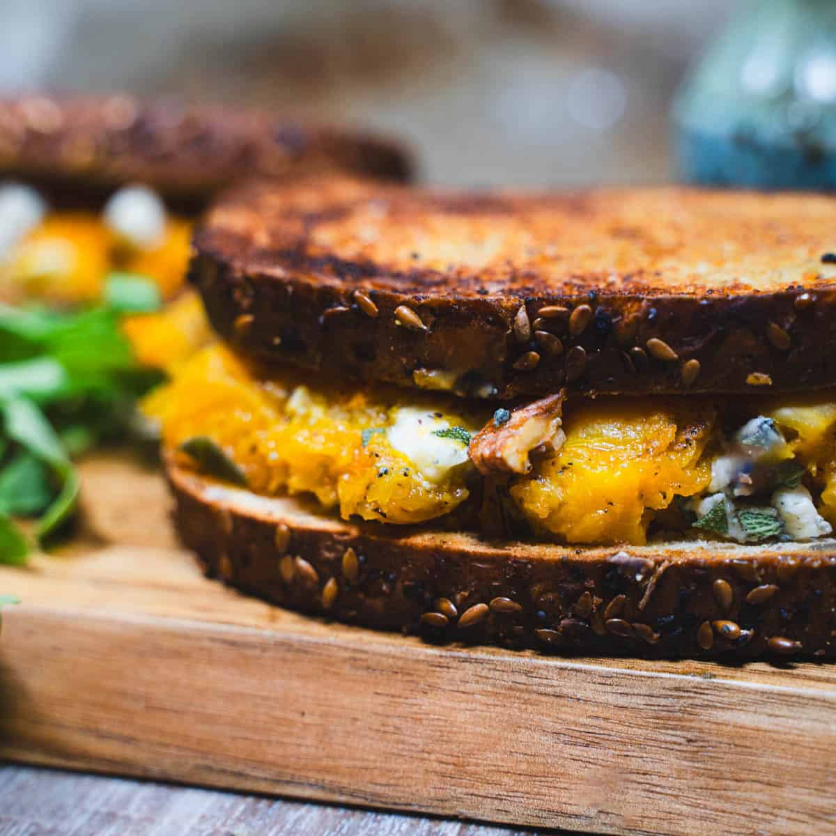 Adult Grilled Cheese with apple and brown sugar butternut squash on a wooden cutting board garnished with arugula.