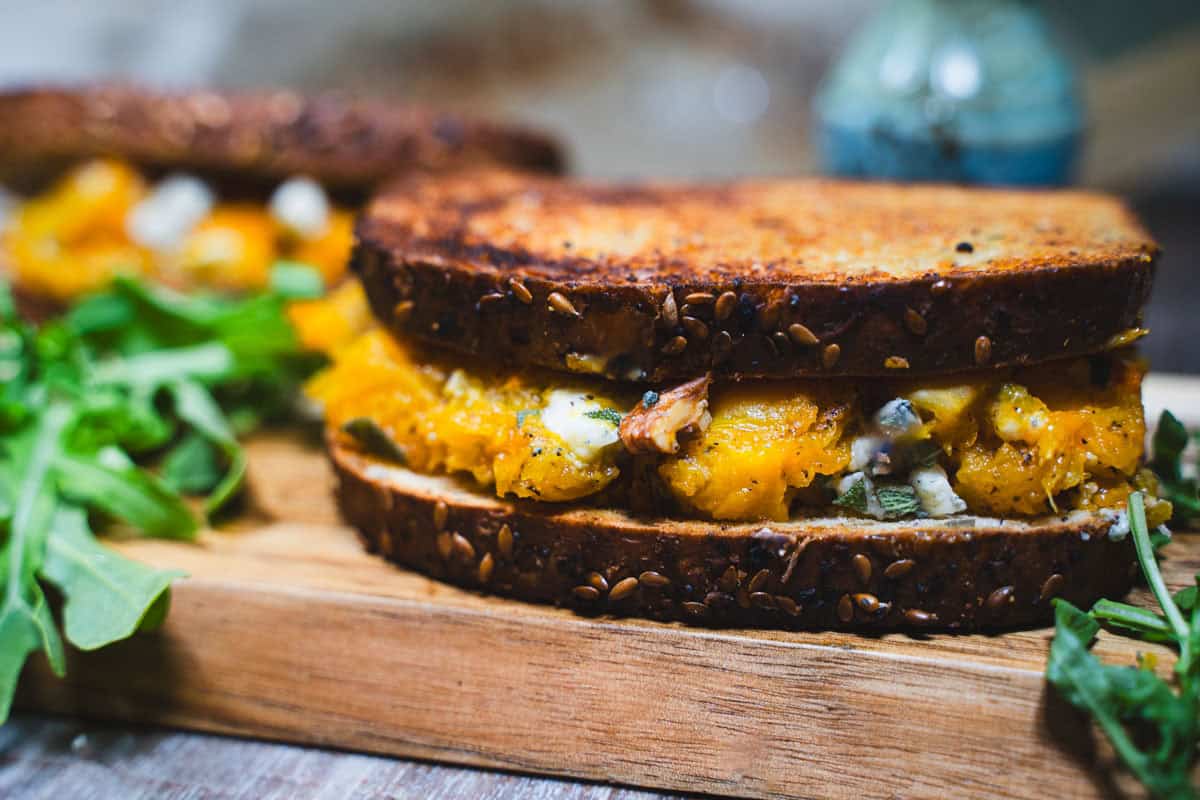 Adult Grilled Cheese with apple and brown sugar butternut squash on a wooden cutting board garnished with arugula.