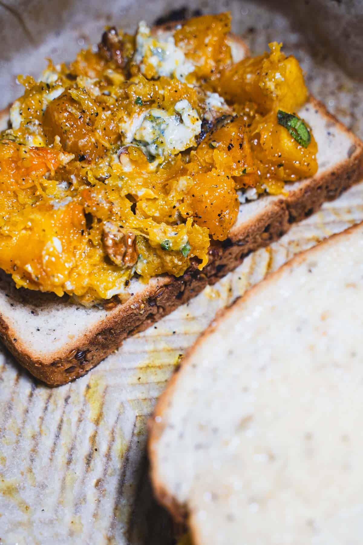 Mashed brown sugar butternut squash on a slice of bread on a baking sheet for adult grilled cheese.