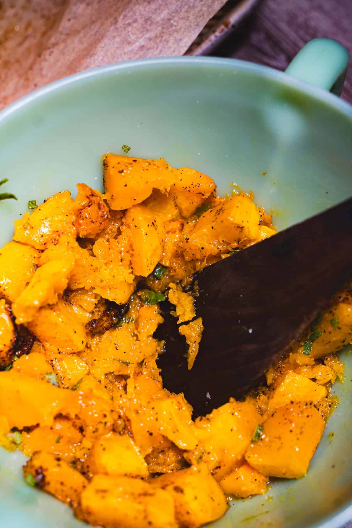 Brown sugar Butternut squash in a green pyrex dish mashed with a wooden spatula for adult grilled cheese.
