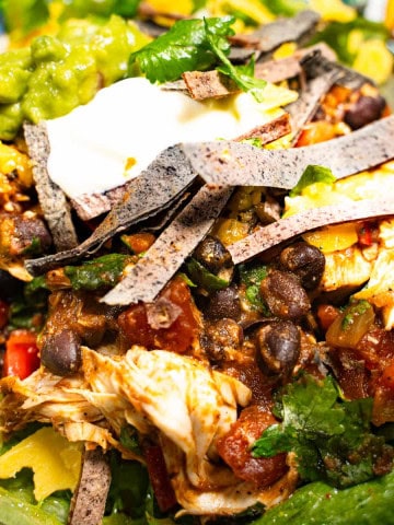 Gluten-free chicken taco salad in a bowl with crispy baked corn tortilla strips, guacamole and sour cream as garnishes.