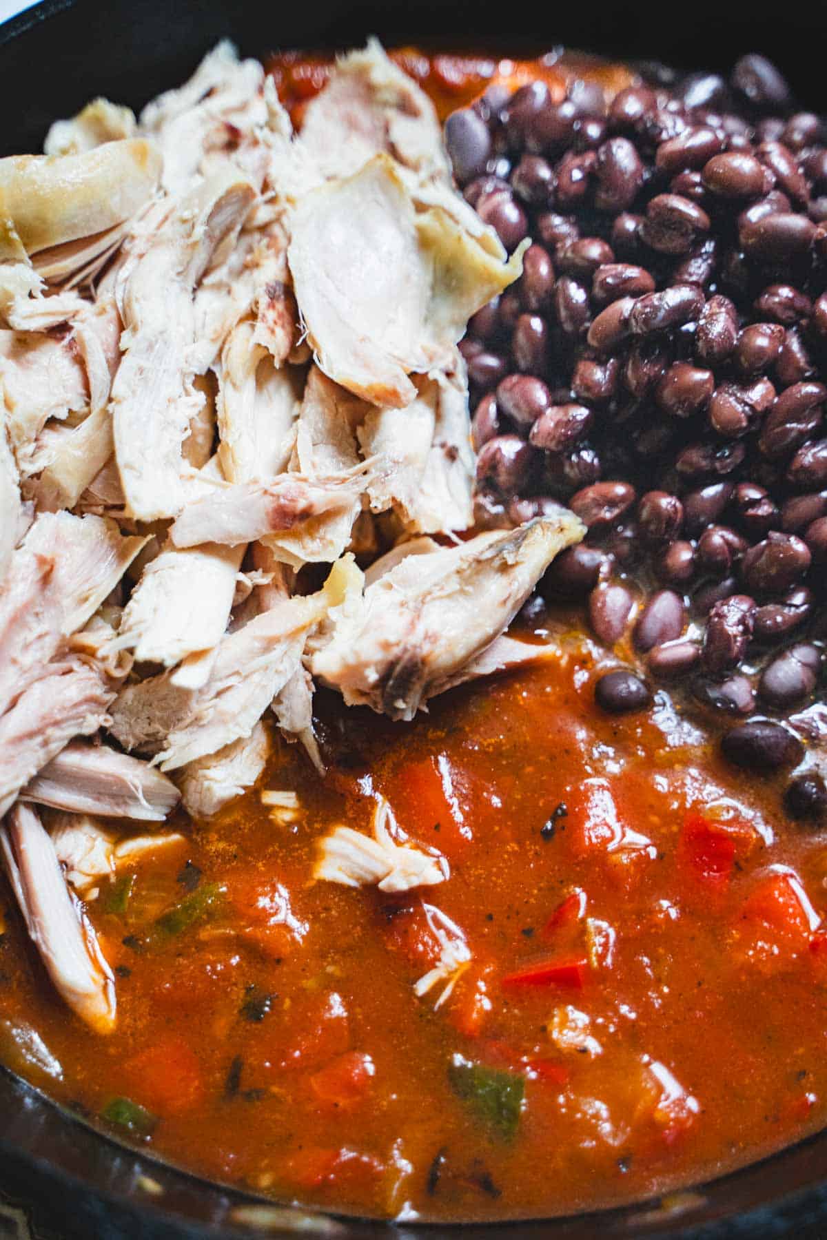Taco salad sauce, shredded rotisserie chicken and black beans in a cast iron skillet.
