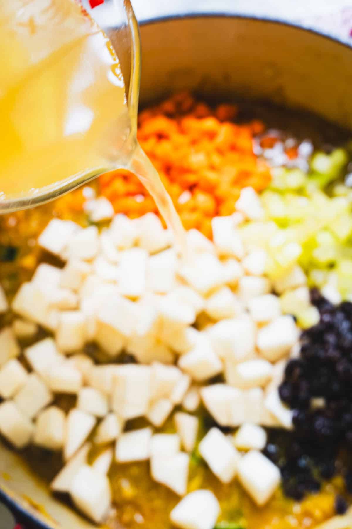 Broth being poured over the hearty vegetables in the dutch oven for the tagine recipe.