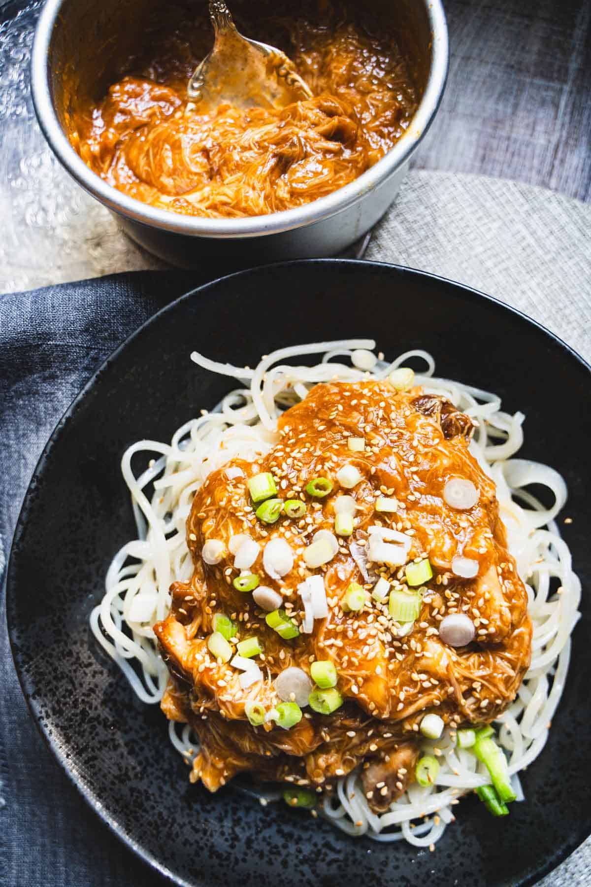 Crock pot chicken and noodles with huli huli sauce in a black bowl garnished with sesame seeds and thinly sliced green onions.