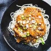 Crock pot chicken and noodles with huli huli sauce in a black bowl garnished with sesame seeds and thinly sliced green onions.