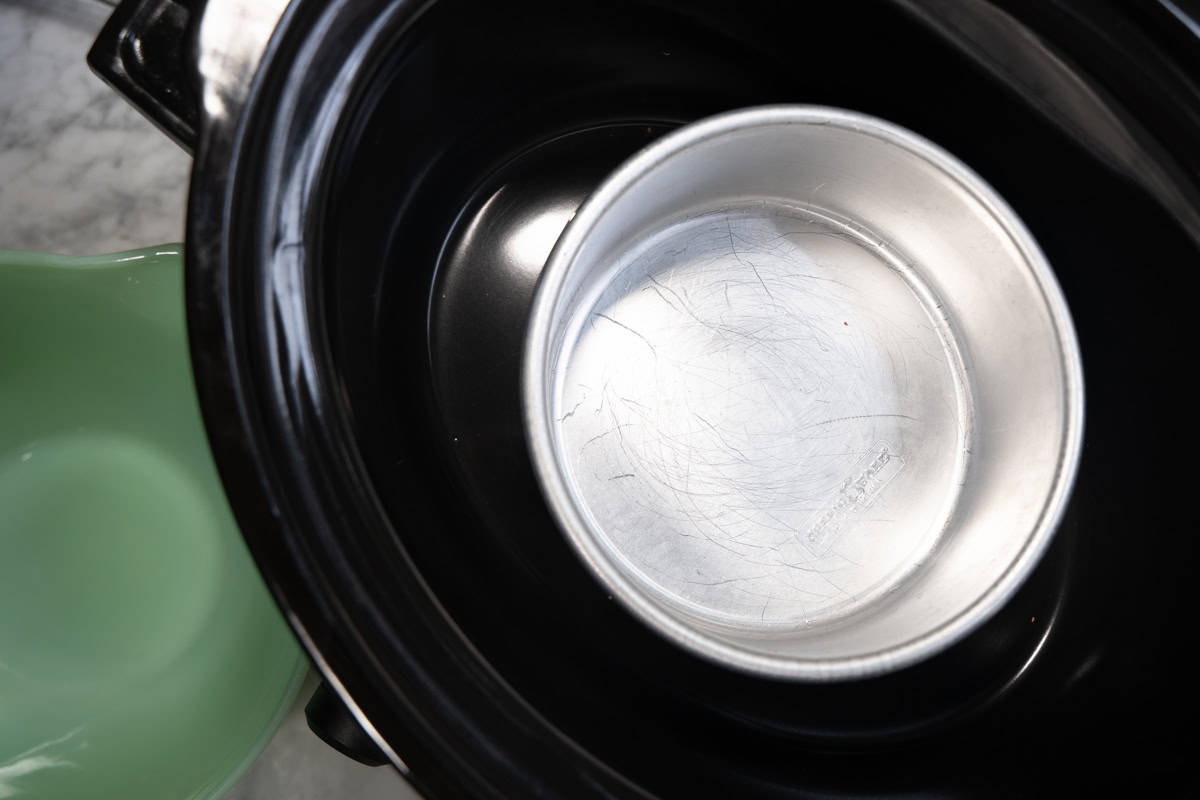 A 6-inch round cake pan placed inside a black liner of a large crockpot to make a small batch of huli huli chicken.