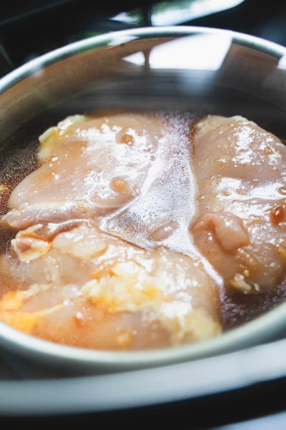 Chicken cooking in huli huli sauce in a covered crockpot inside a small baking dish.