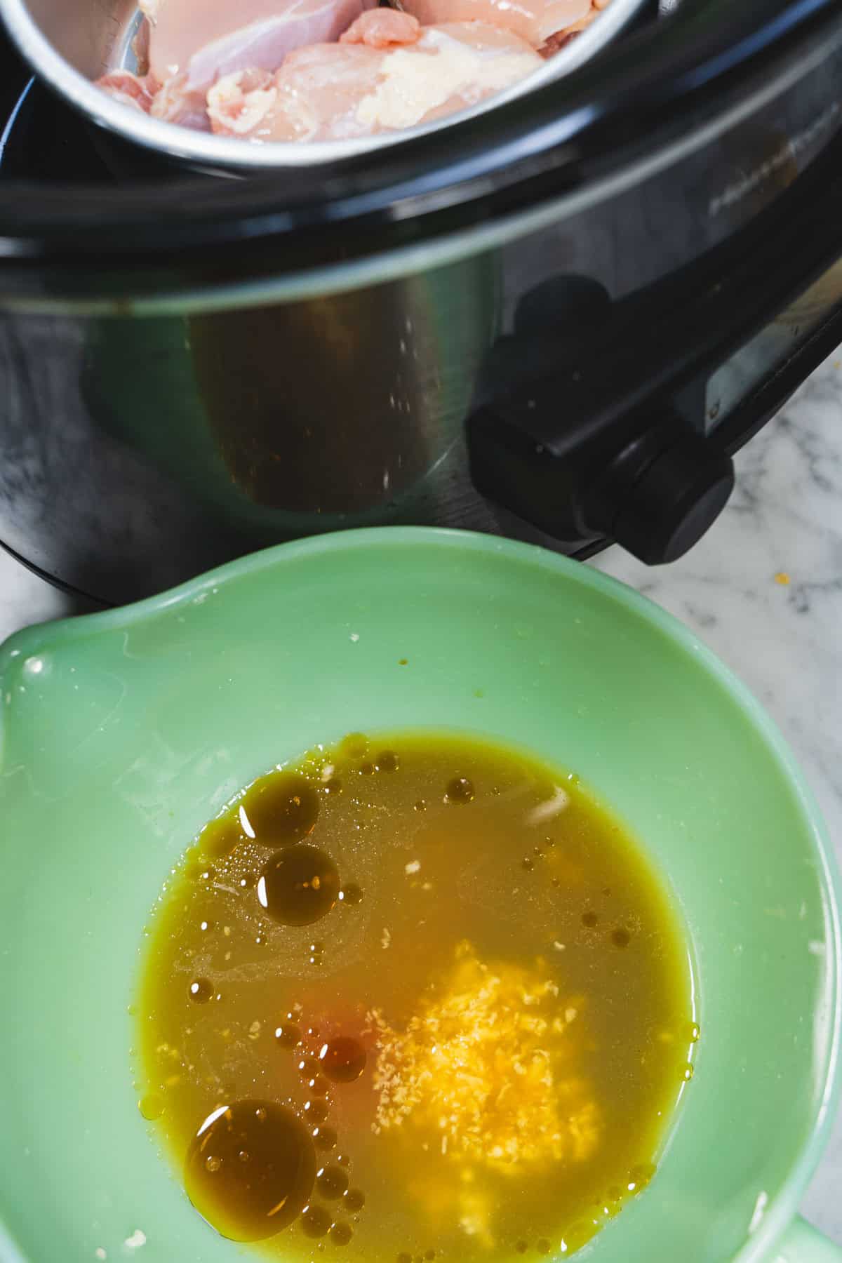 Huli Huli chicken sauce ingredients in a green mixing bowl next to a large crockpot with a small baking dish inserted and chicken nestled into the baking dish.