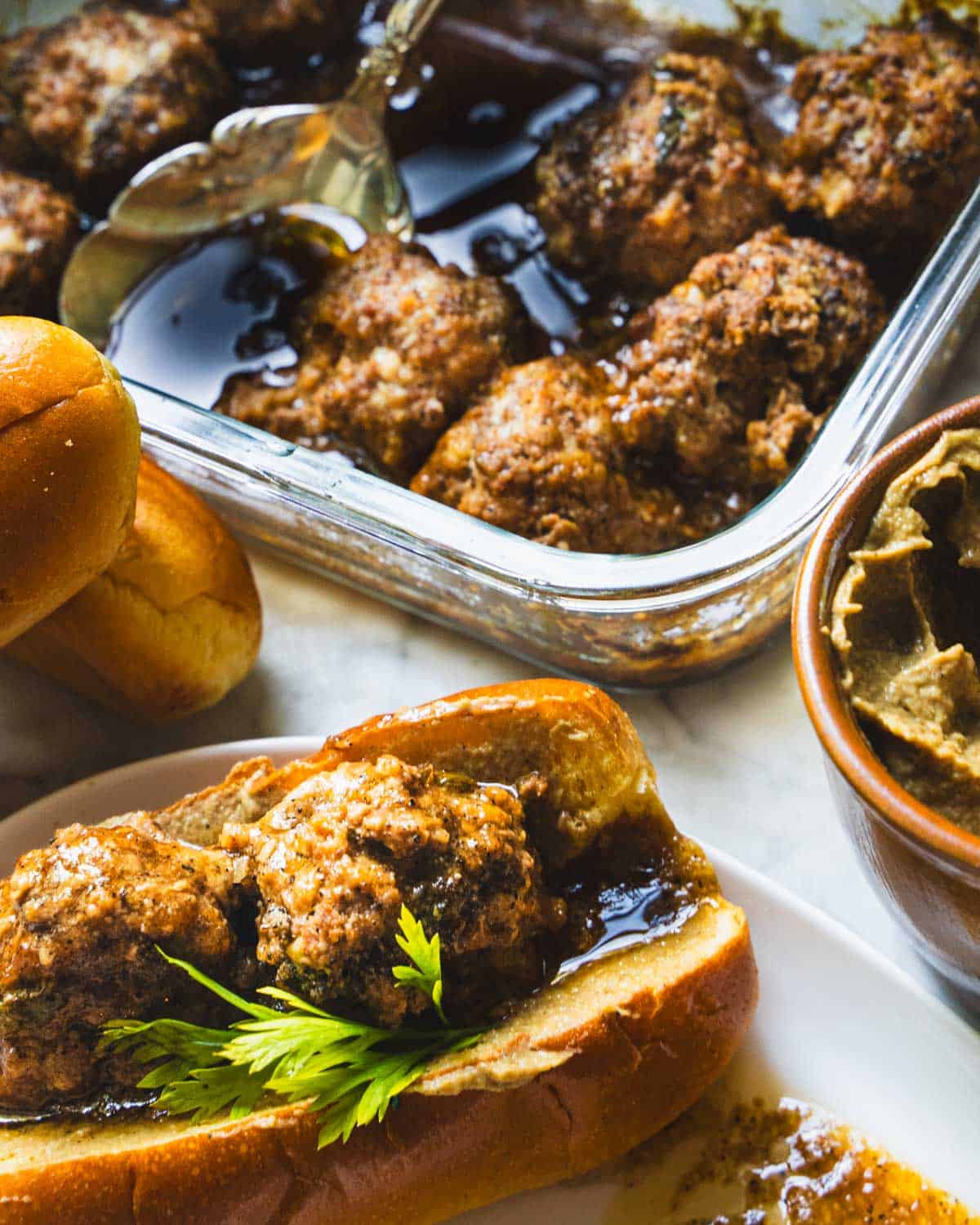 Meatloaf meatballs in a black pepper sauce in a baking dish alongside meatloaf meatballs sandwich of hot dog bun.