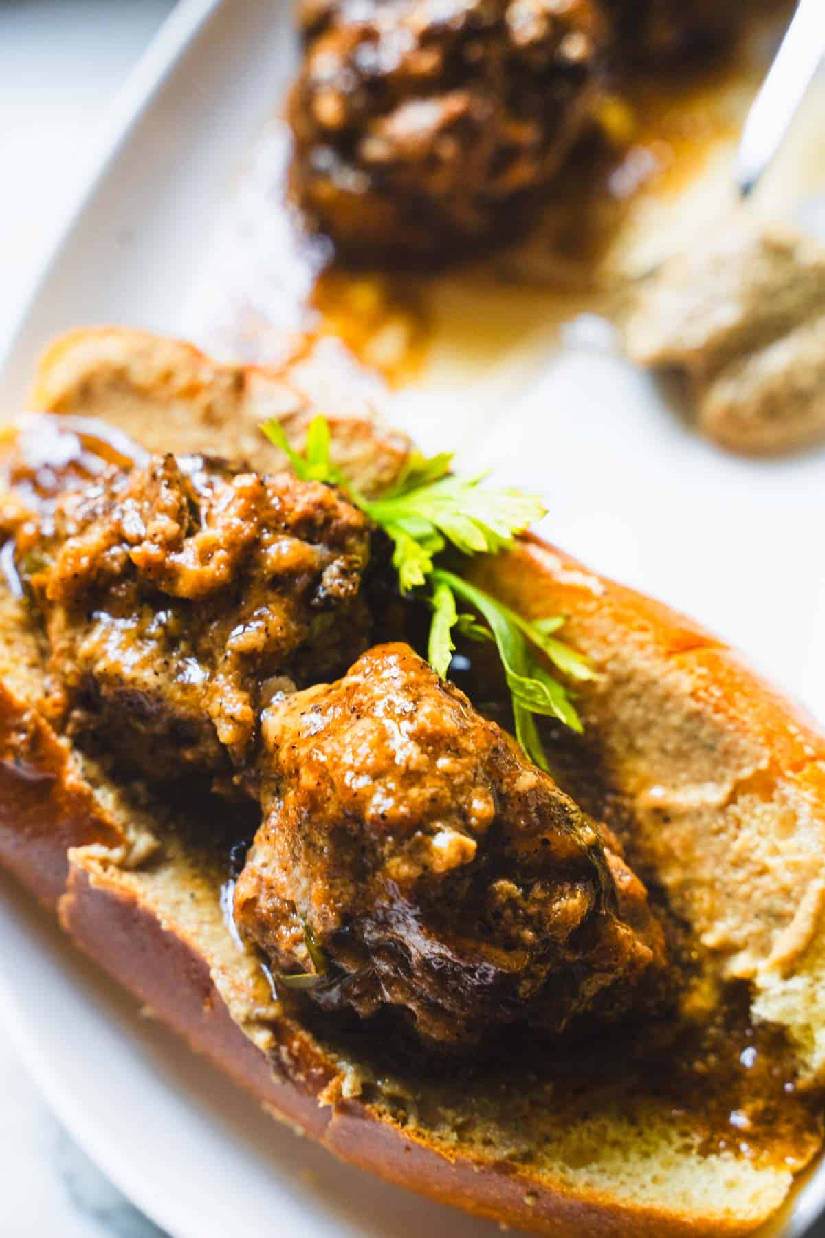 Meatball sandwich in sauce on a white plate garnished with parsley.