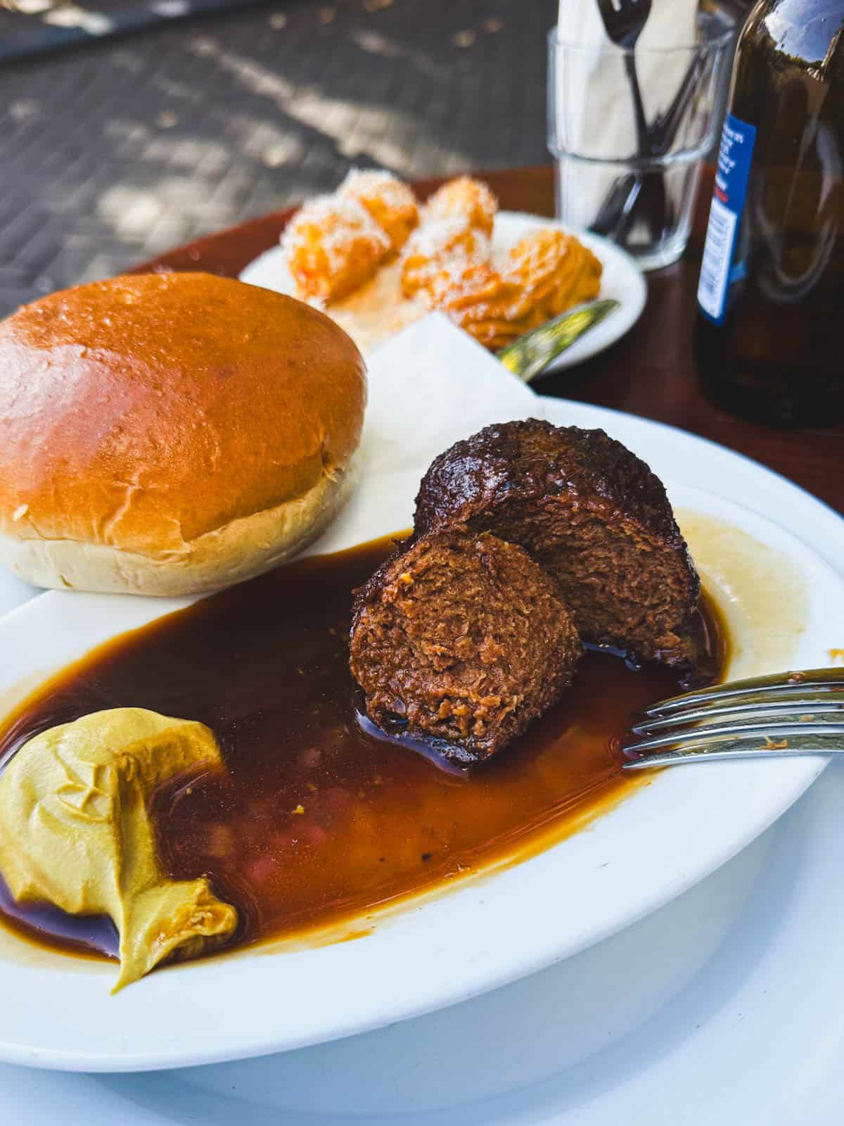 Meatloaf meatballs in sauce on a white plate served with black pepper sauce, mustard and a brioche bun.