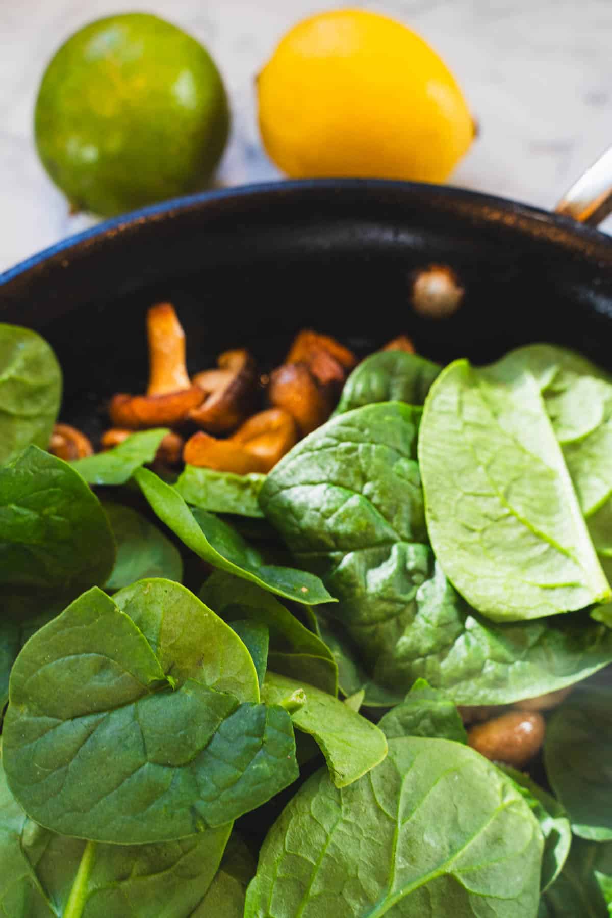 Spinach and mushrooms in a black saute pan for the red thai coconut spinach tomato curry soup.