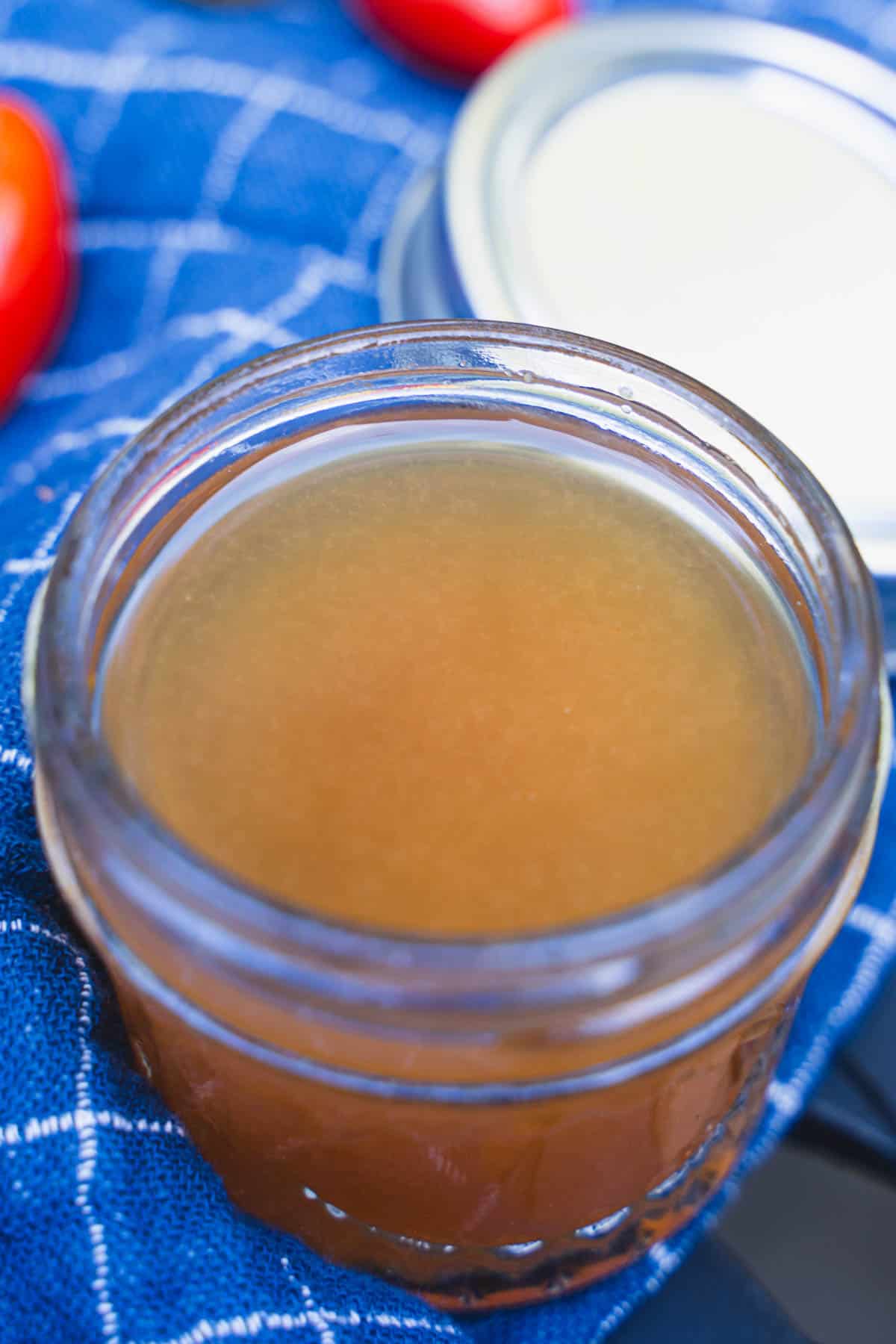 Tomato Essence in a small glass mason jar on a blue checked background alongside cherry tomatoes.