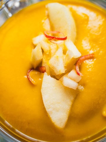 apple autumn squash soup in a glass mug on a flowered plate garnished with diced apple.