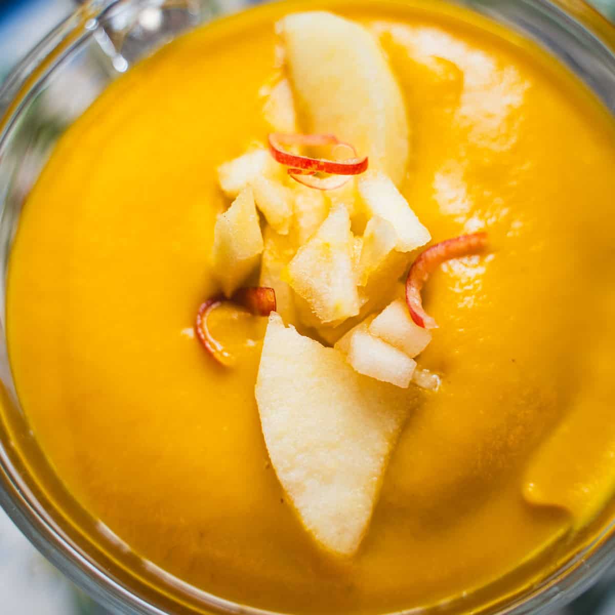 apple autumn squash soup in a glass mug on a flowered plate garnished with diced apple.