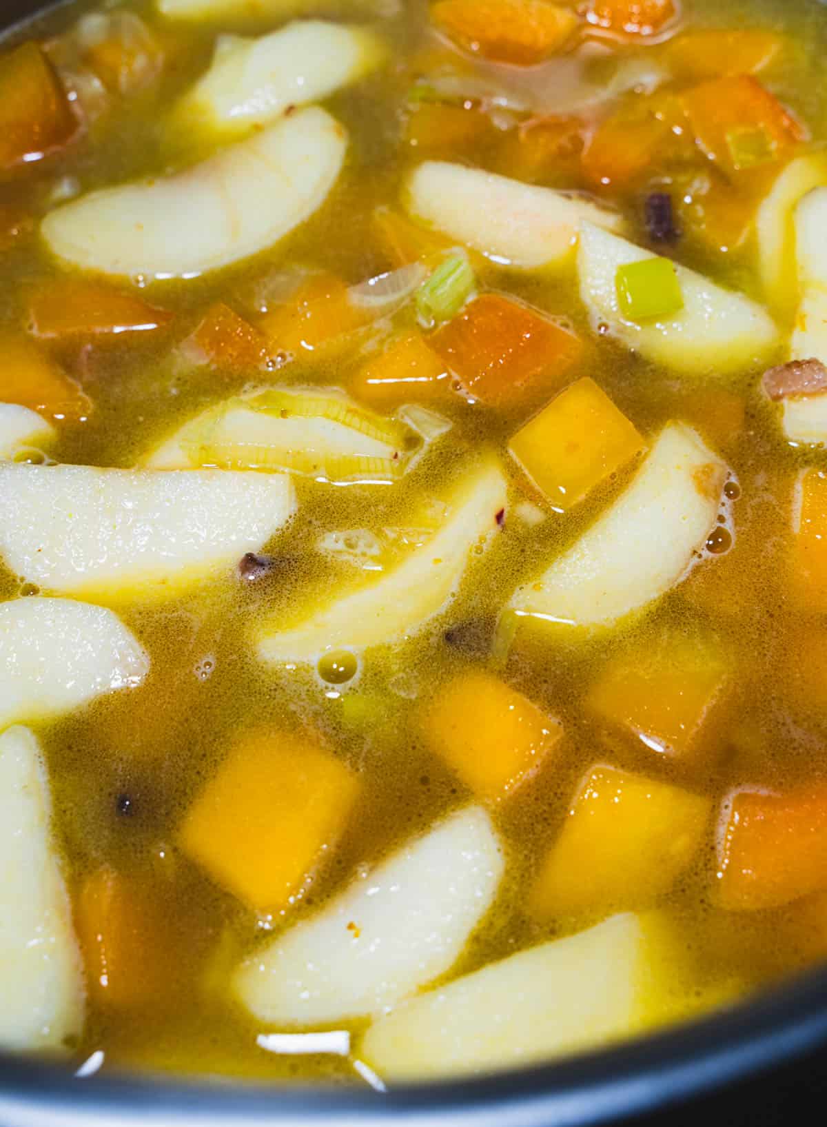 Apples, butternut squash, leeks and bacon, simmering in apple cider in a large soup pot for Apple and Autumn Squash Soup.