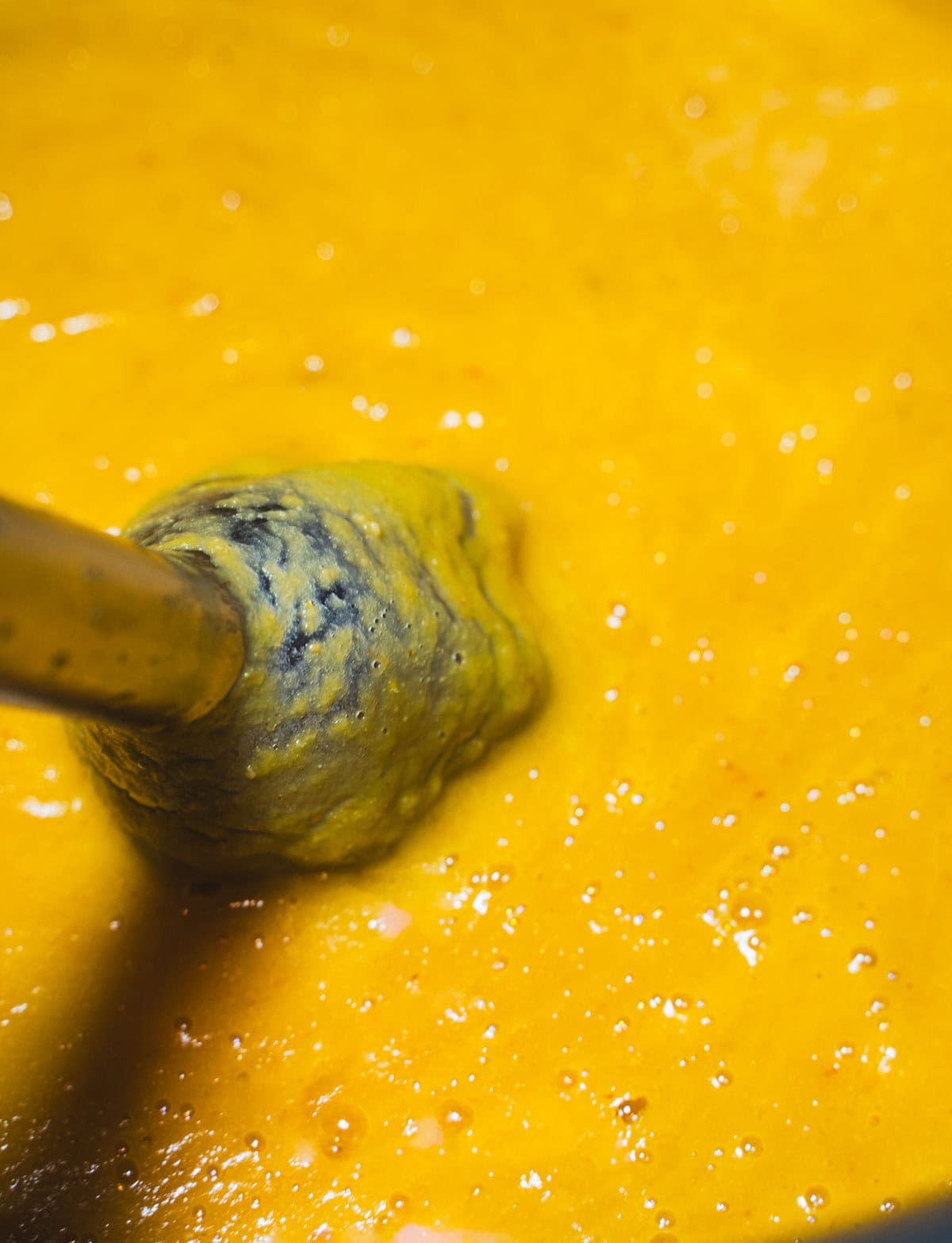 A immersion blender in the soup pot blending the Autumn Squash Soup with Apples and Leeks until smooth.