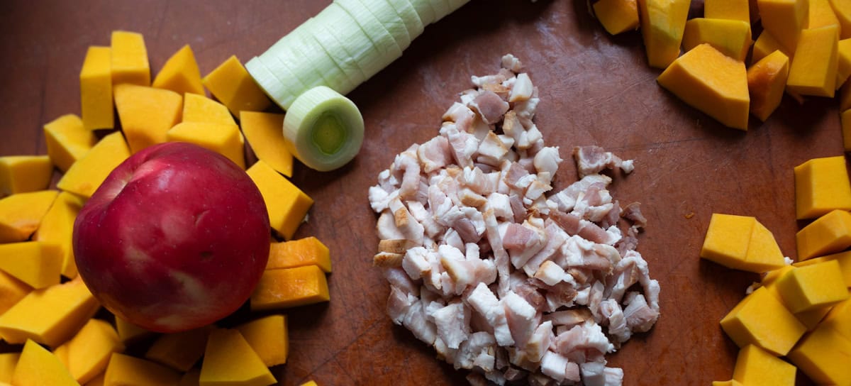 Apple, chopped bacon, sliced leek and cubed butternut squash on brown cutting board to make a Apple and Butternut Squash Soup