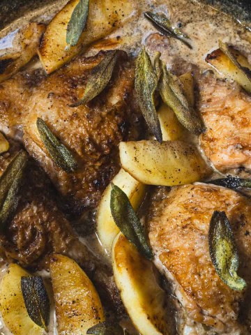 Braised chicken thighs and legs in a cast iron skillet with apples and a chicken normandy sauce.