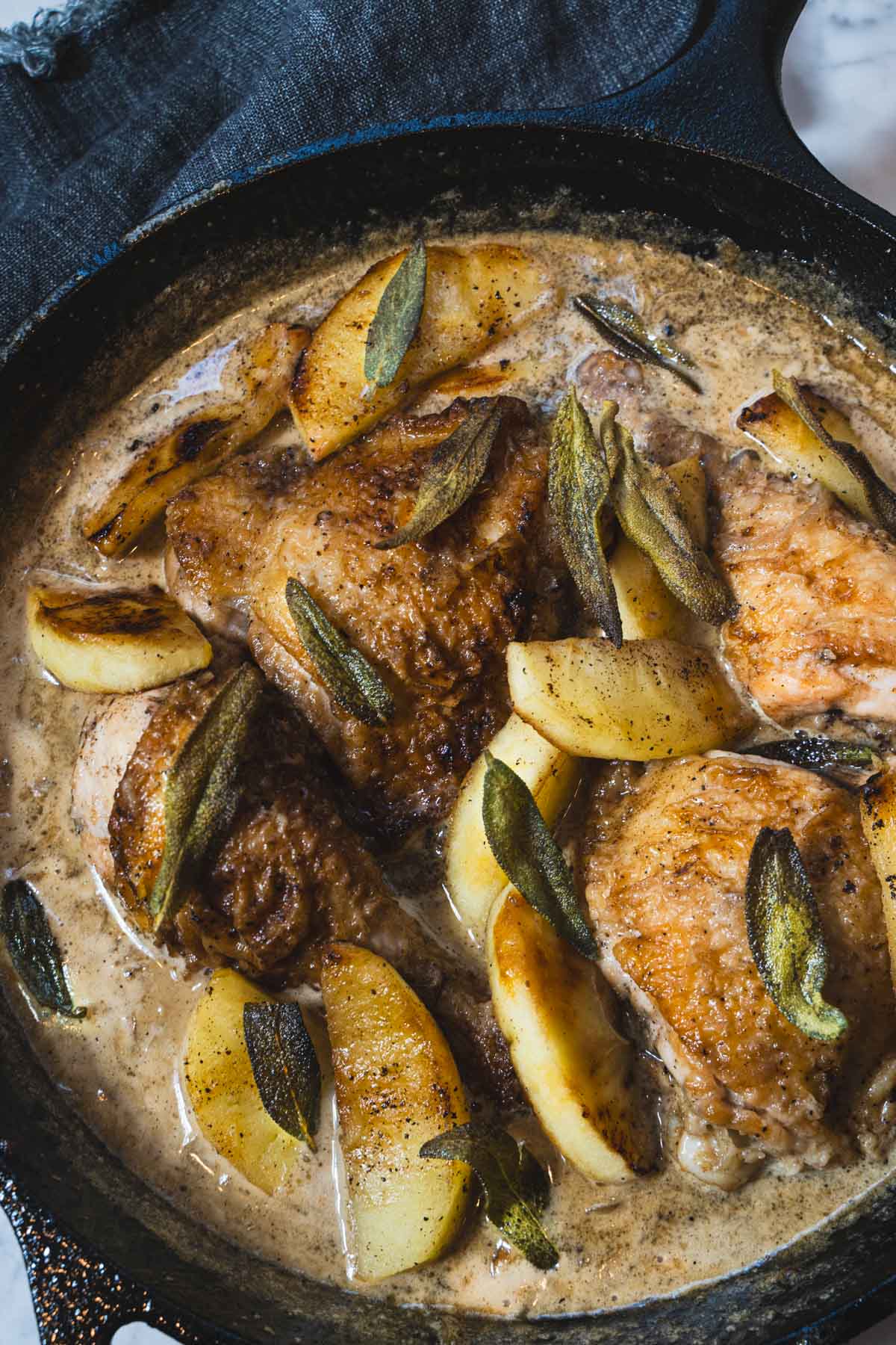 Braised chicken thighs and legs in a cast iron skillet with apples and a chicken normandy sauce.