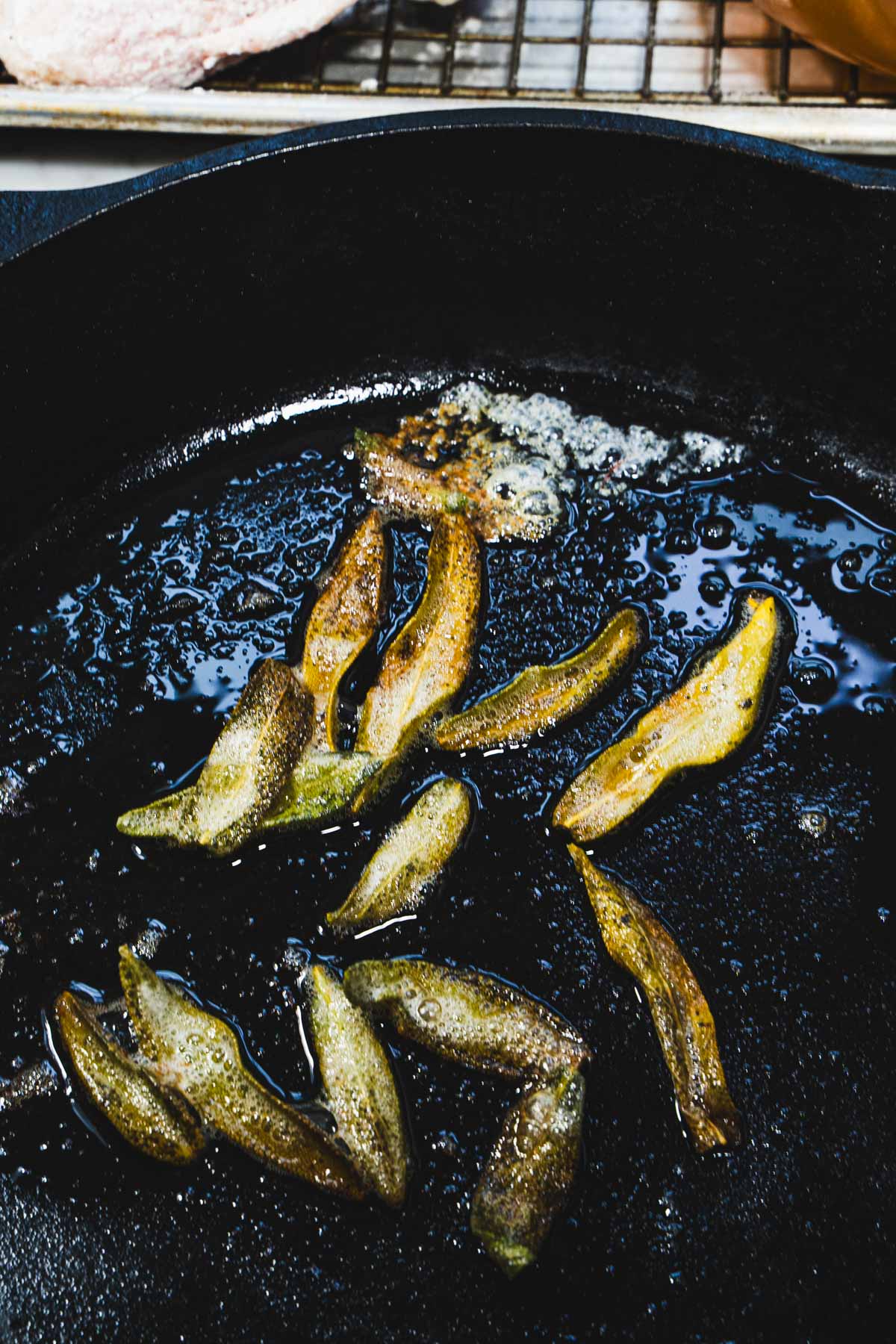 Browned sage leaves in a cast iron skillet for Chicken Normandy.