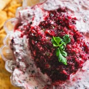 Cranberry and Jalapeno dip with cream cheese in a clear glass serving bowl surrounded by pita chips.