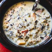 cream of mushroom wild rice soup in a brown bowl with a spoon on a red plate.