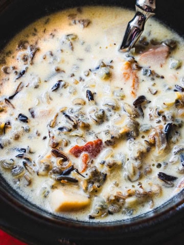 cream of mushroom wild rice soup in a brown bowl with a spoon on a red plate.