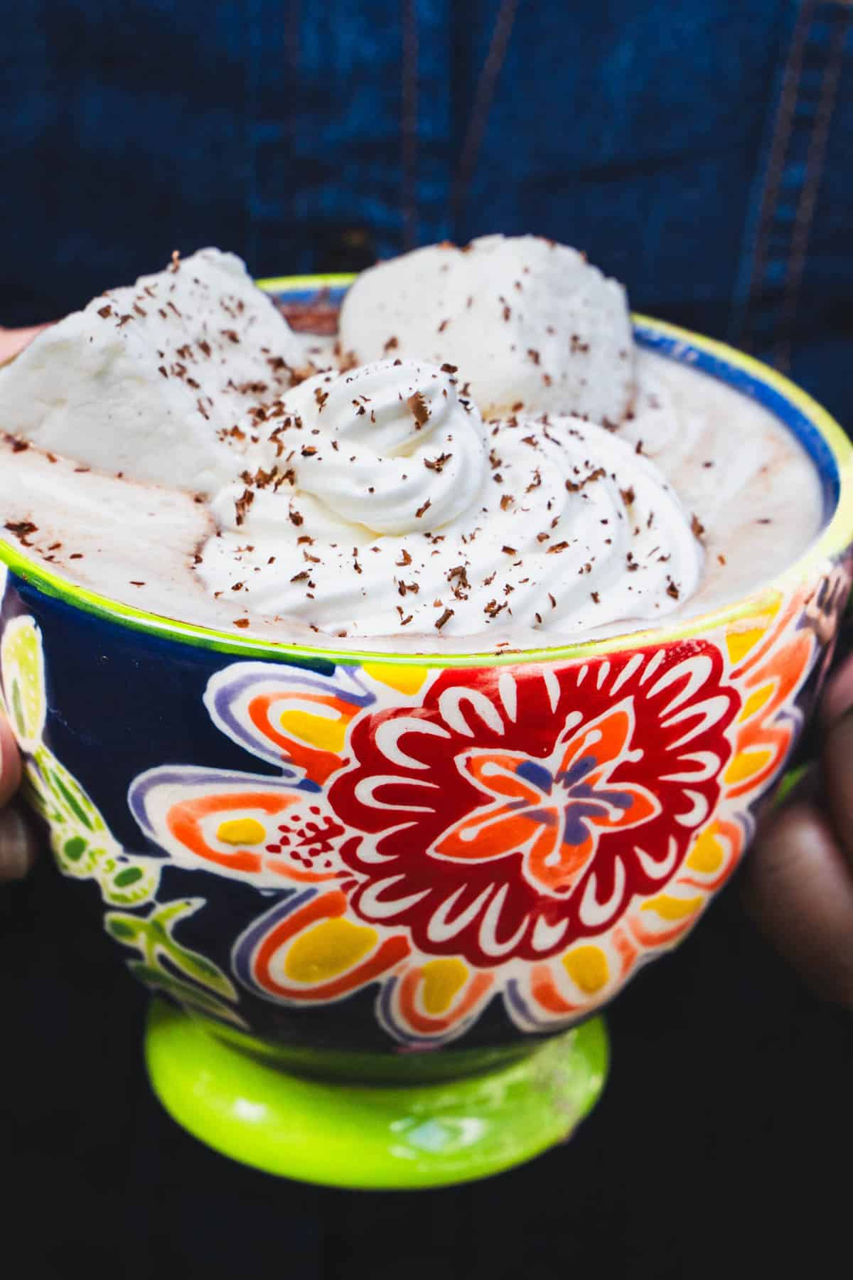 Dark hot chocolate and homemade marshmallows in a blue cup held in a womens hands.