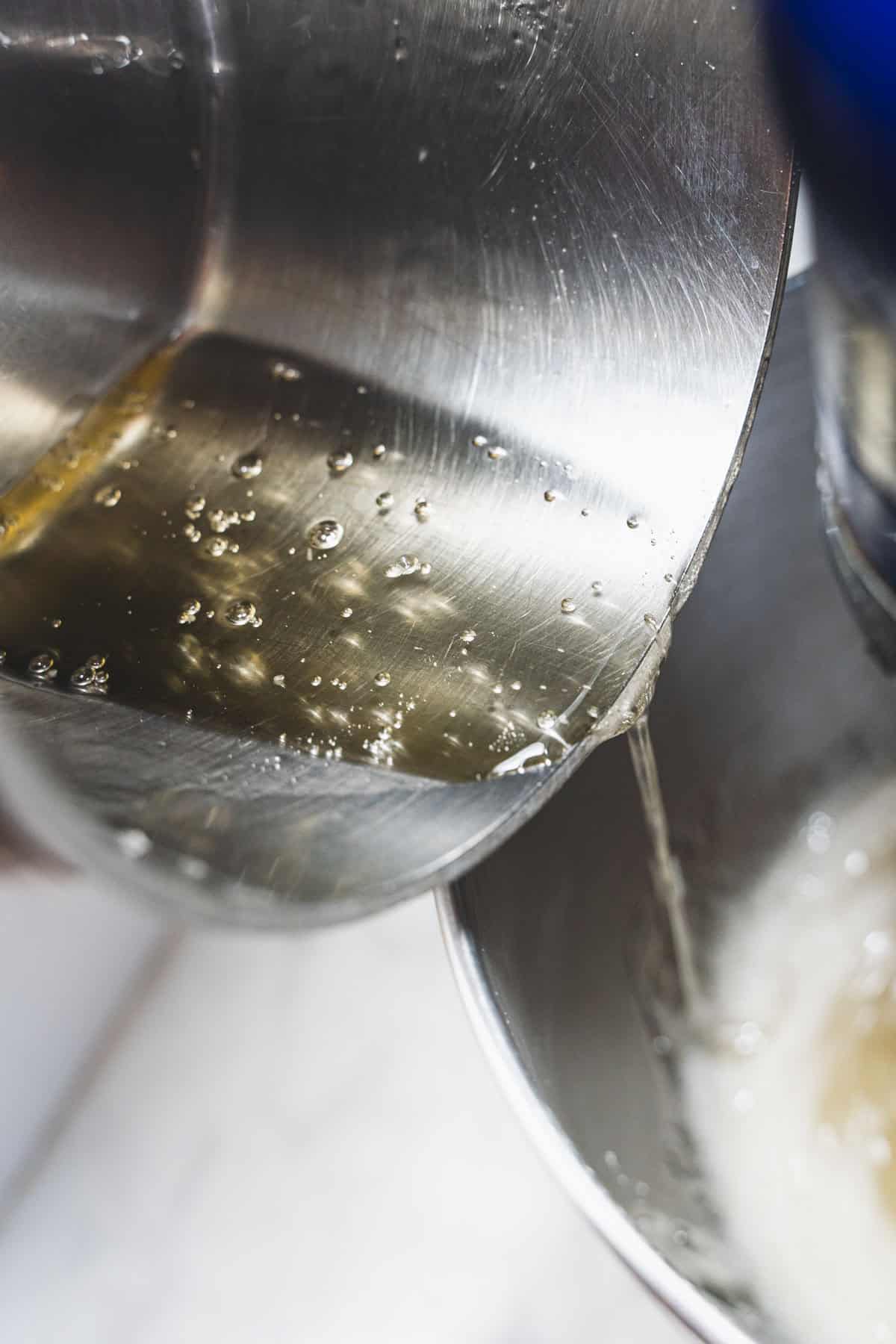 Sugar syrup in saucepan being poured into stand mixer bowl over gelatin.