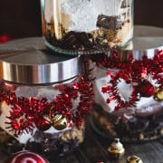 Dark hot chocolate mix and homemade marshmallows in a jar decorated with red garland and small gold and red bells.