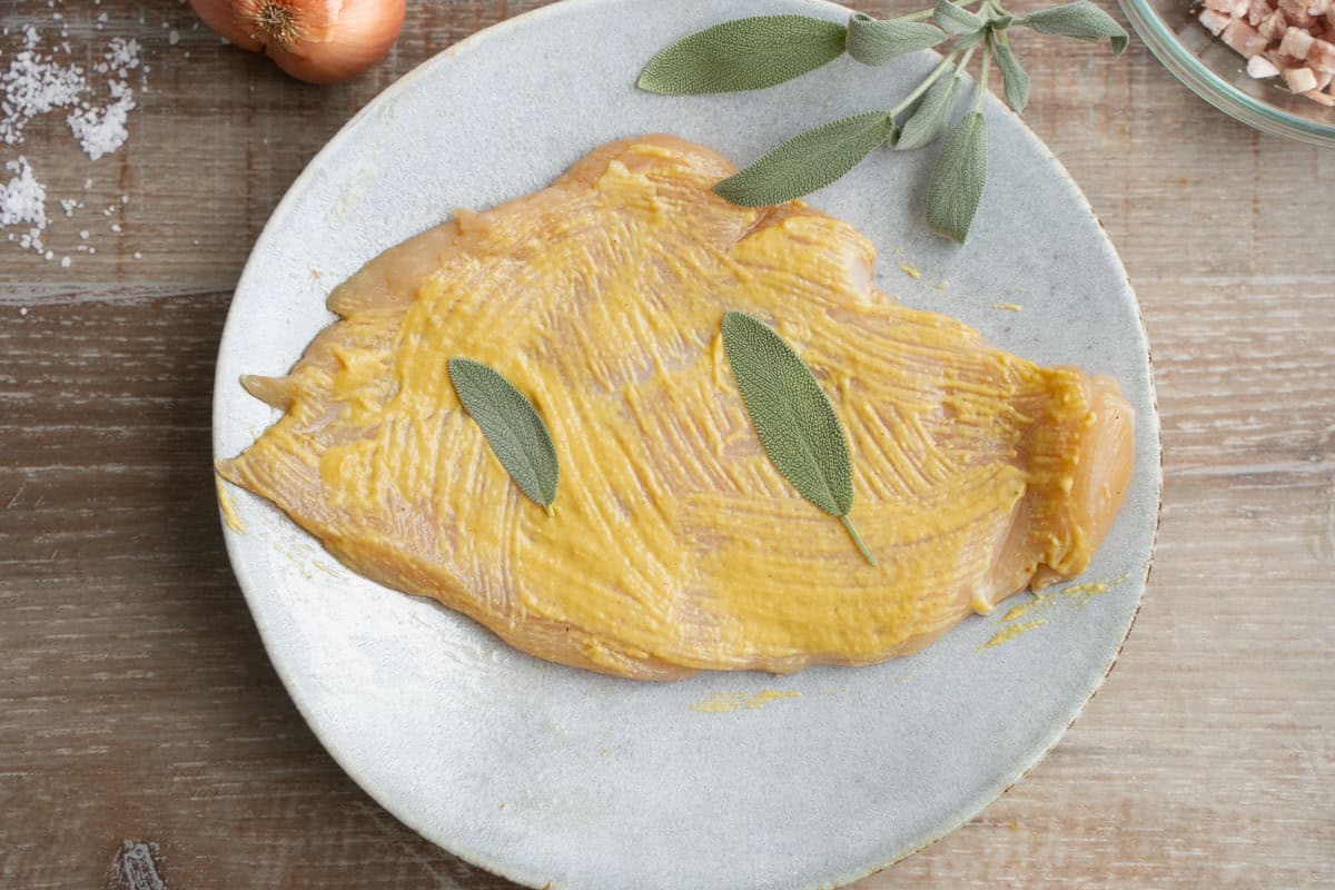 Flattened chicken with mustard spread on top and two sage leaves pressed into the breast for Chicken Marsala Fettuccine.