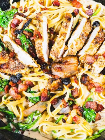 Chicken Marsala Fettuccine in a black cast iron skillet garnished with crispy pancetta and fried sage.