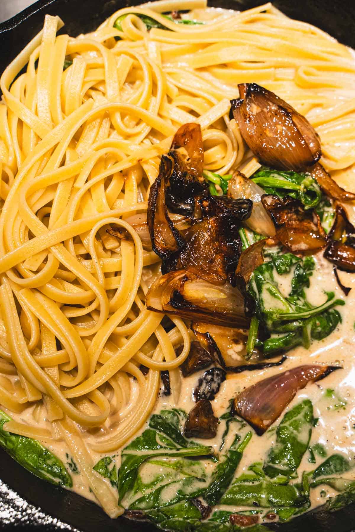 Fettuccine, baslmic-roasted mushrooms and shallots, fresh spinach in marsala sauce in a black cast iron skillet.