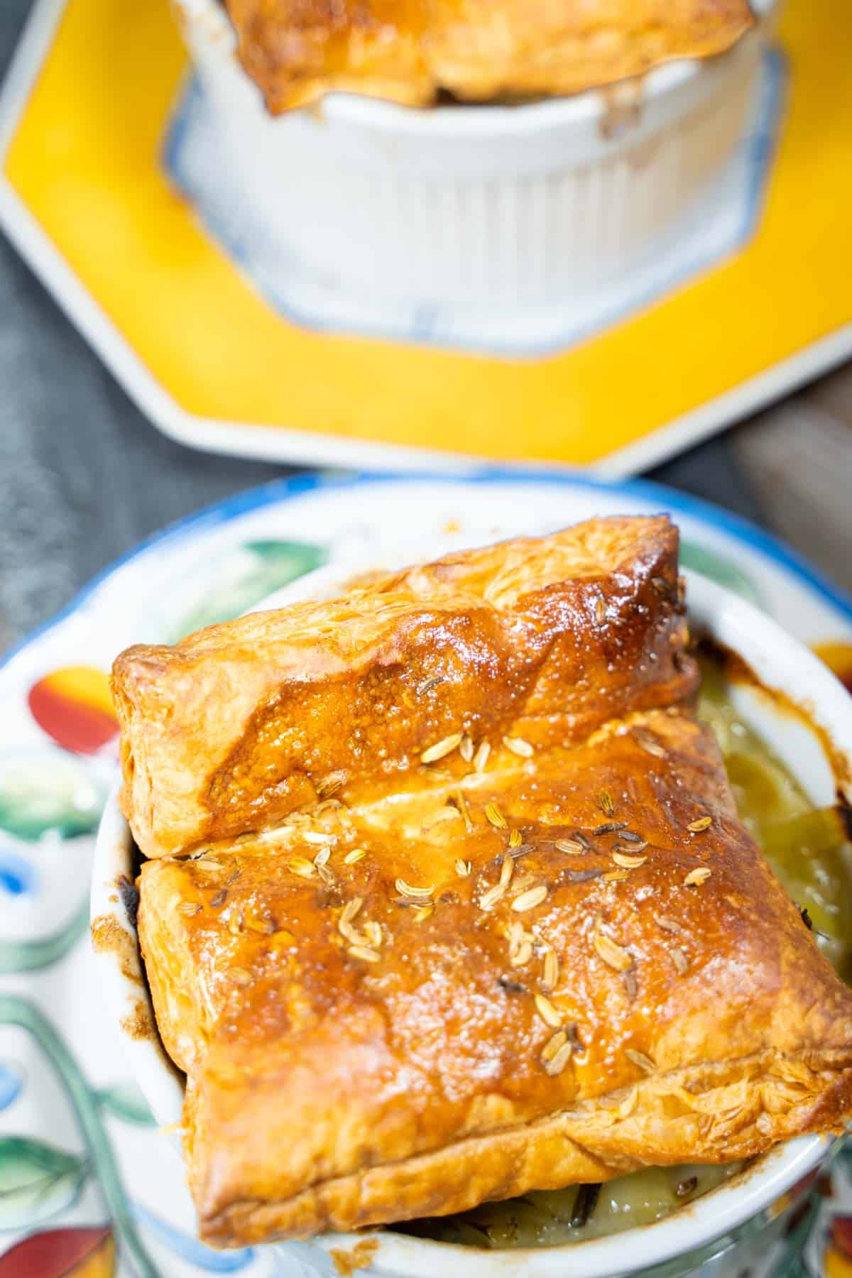 Individual puff pastry chicken pot pies with a square puff pastry top served in ramekins on serving plates.