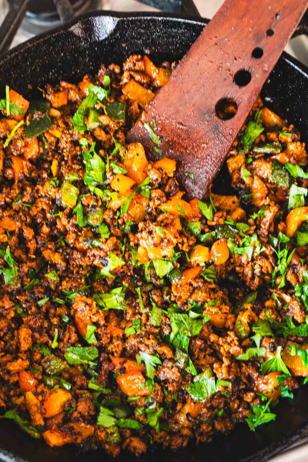 Chorizo and peppers in black cast iron skillet with a wooden spatula for spanish eggs with plant based chorizo and eggs.