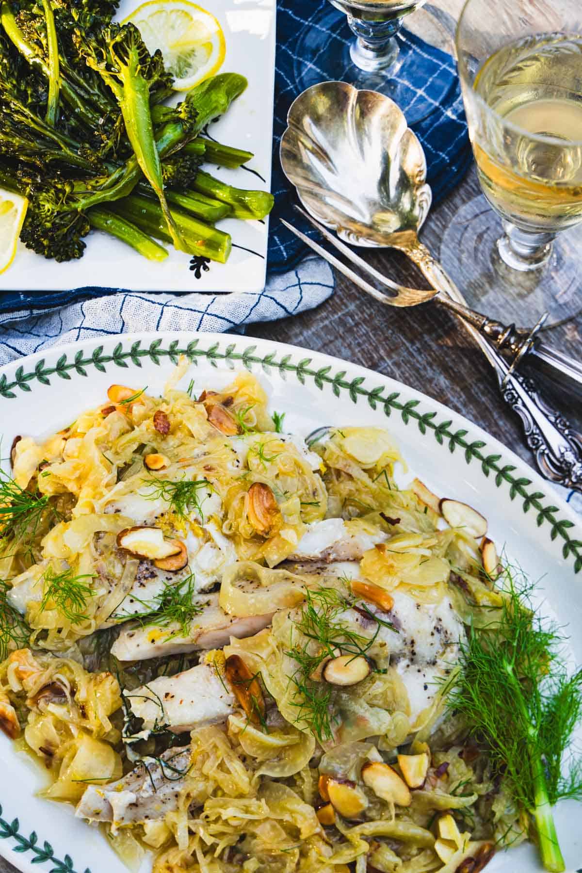 Sous vide yellowtail fish on a leeks and fennel white sauce on a white platter with sauteed broccolini on a white plate.