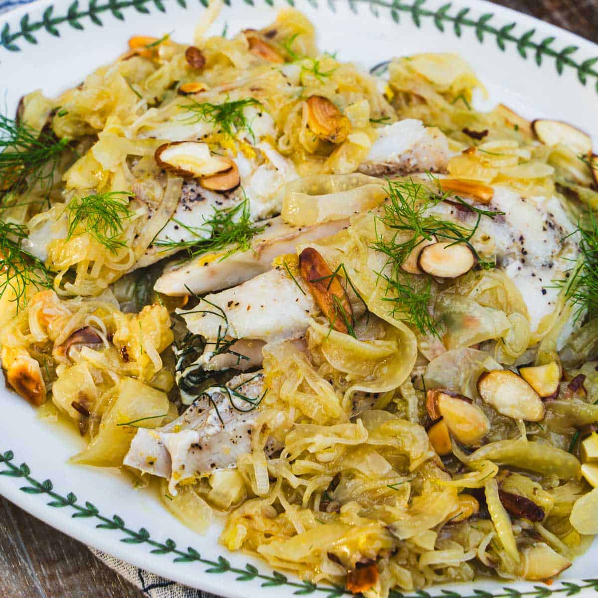 Sous vide yellowtail fish recipe on a white platter with a white sauce of leeks and onions garnished with toasted almonds on a white platter.