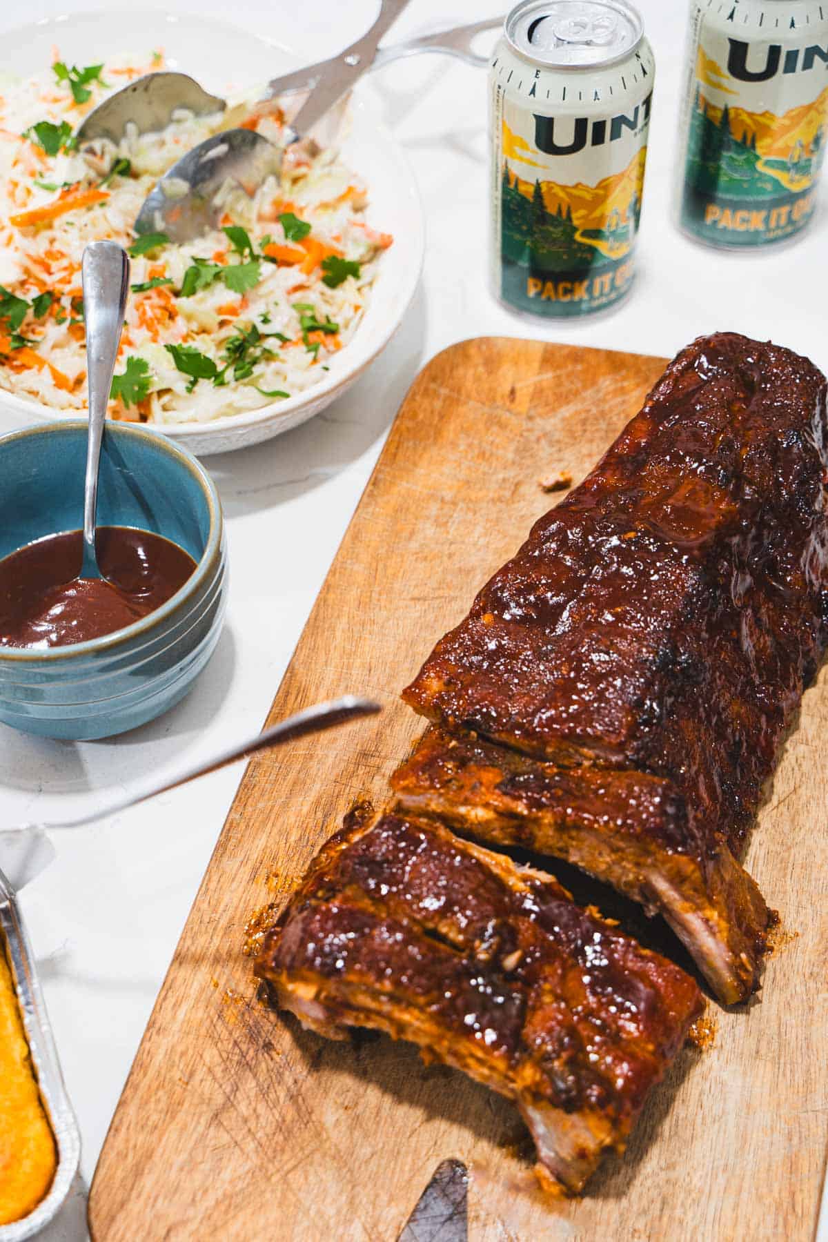 Fall off the bone sticky ribs on a cutting board with sides of coleslaw, bbq sauce and 2 cans of beer.