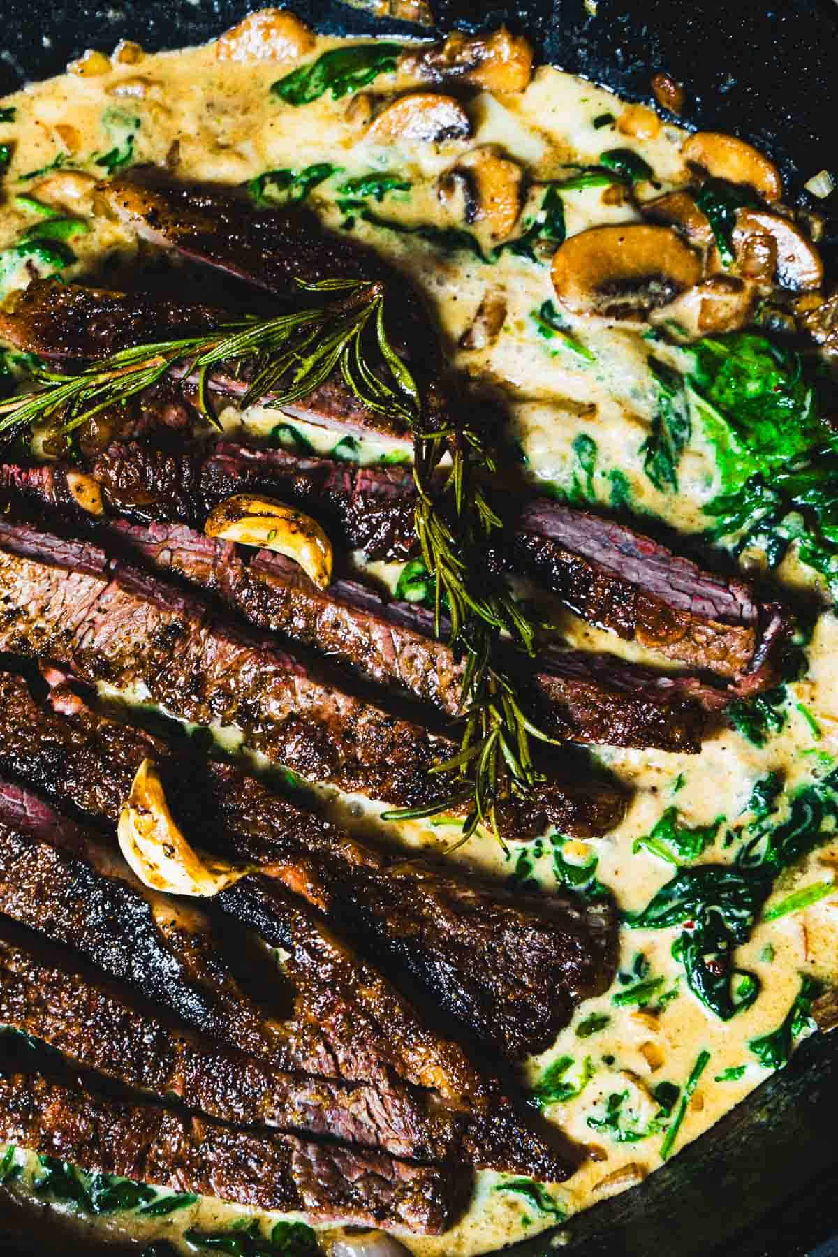 one skillet ribe eye steak dinner with steakhouse creamed spinach and mushrooms in a cast iron skillet.