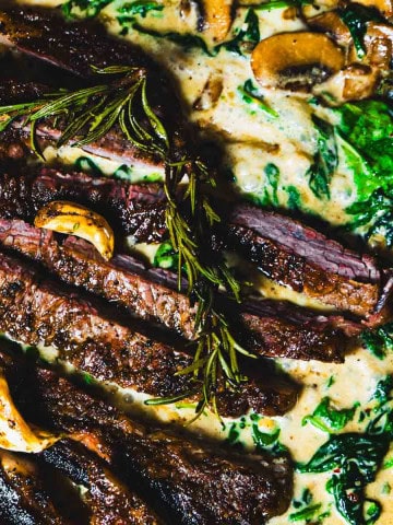 one skillet ribe eye steak dinner with steakhouse creamed spinach and mushrooms in a cast iron skillet.