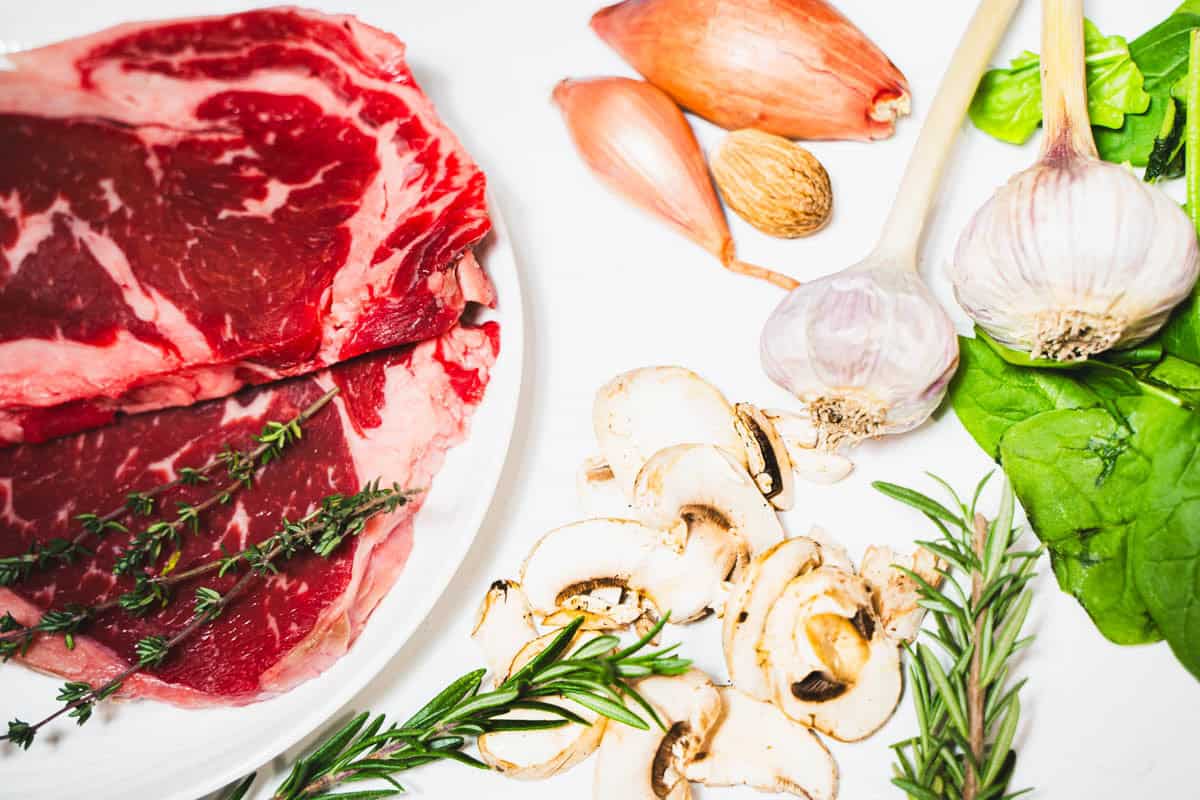 Boneless rib eye steak on white platter with herbs and garlic for one skillet rib eye dinner.