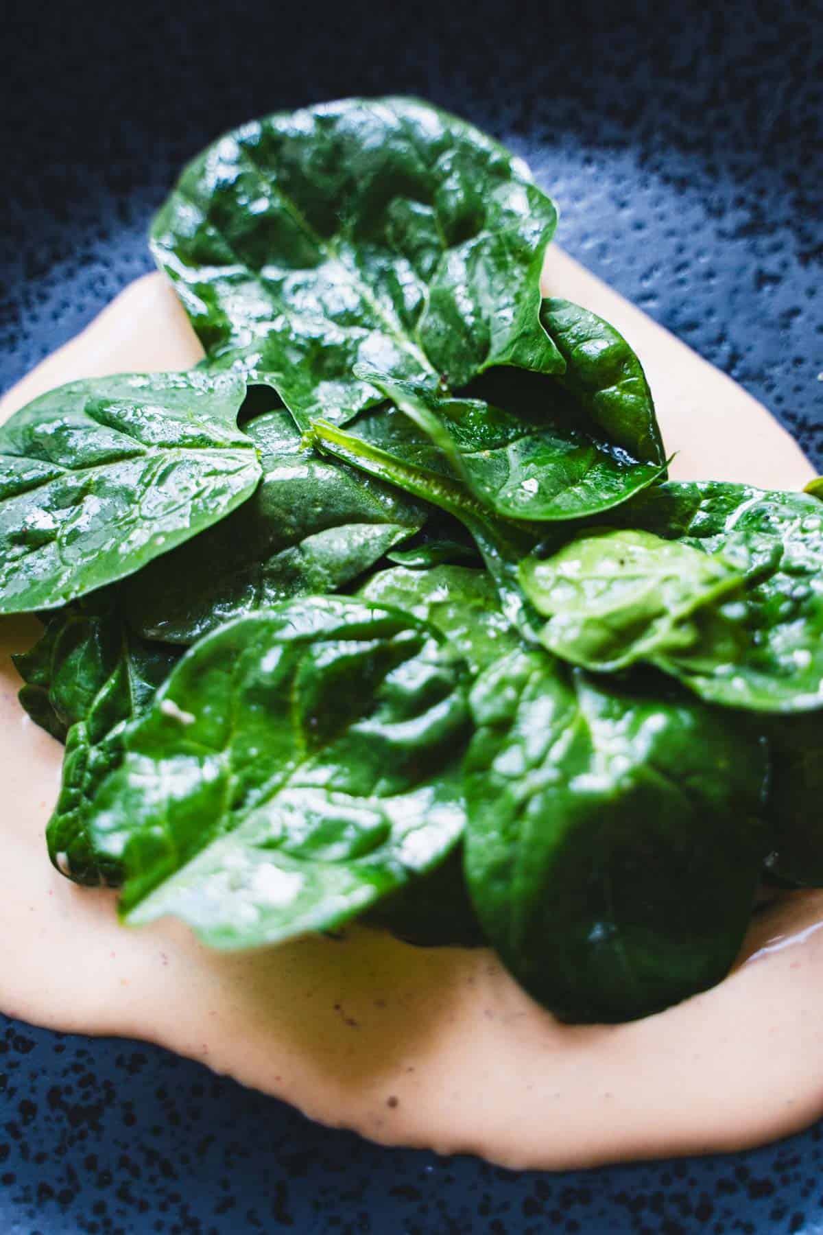 Lightly dressed spinach salad on top of a pool of chipotle mayo for roasted beets and sweet potato hash with eggs.